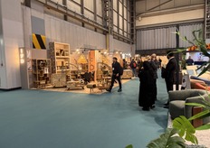 The vibrant entrance to Hall 5 welcomes visitors into a dynamic space where lively discussions unfold amid a stunning display of innovative furniture and a captivating floor illuminated with colorful lights.